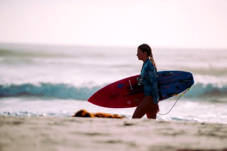 woman carrying red and blue surfboard walking on shore during daytime photo