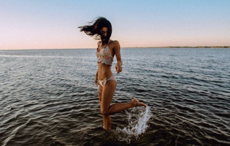 A girl in a bikini flicks her leg up behind her in the water at a beach photo