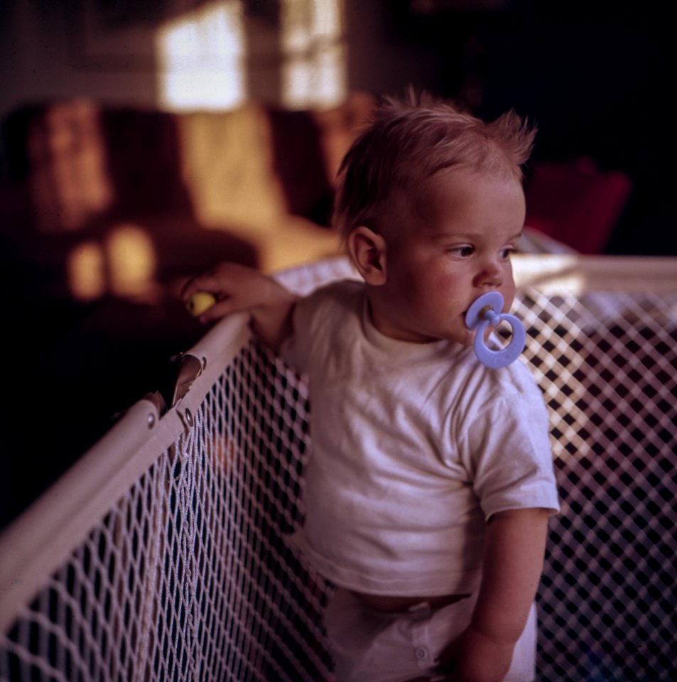 baby with purple pacifier standing on crib photo