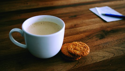shallow focus photography of white ceramic mug beside two baked cookies on brown wooden board photo