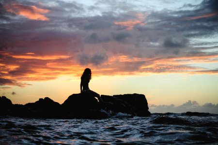 silhouette photo of woman sitting on rock during golden hour photo