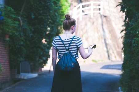 woman in striped shirt with backpack holding sunglasses while walking on street photo