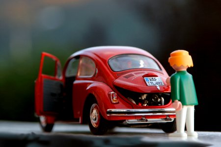 orange hair Lego toy looking at red beetle car photo