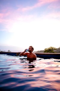 topless man drinking beverage while on swimming pool photo