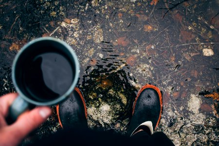 person holding coffee mug with pair of black shoes during daytime photo