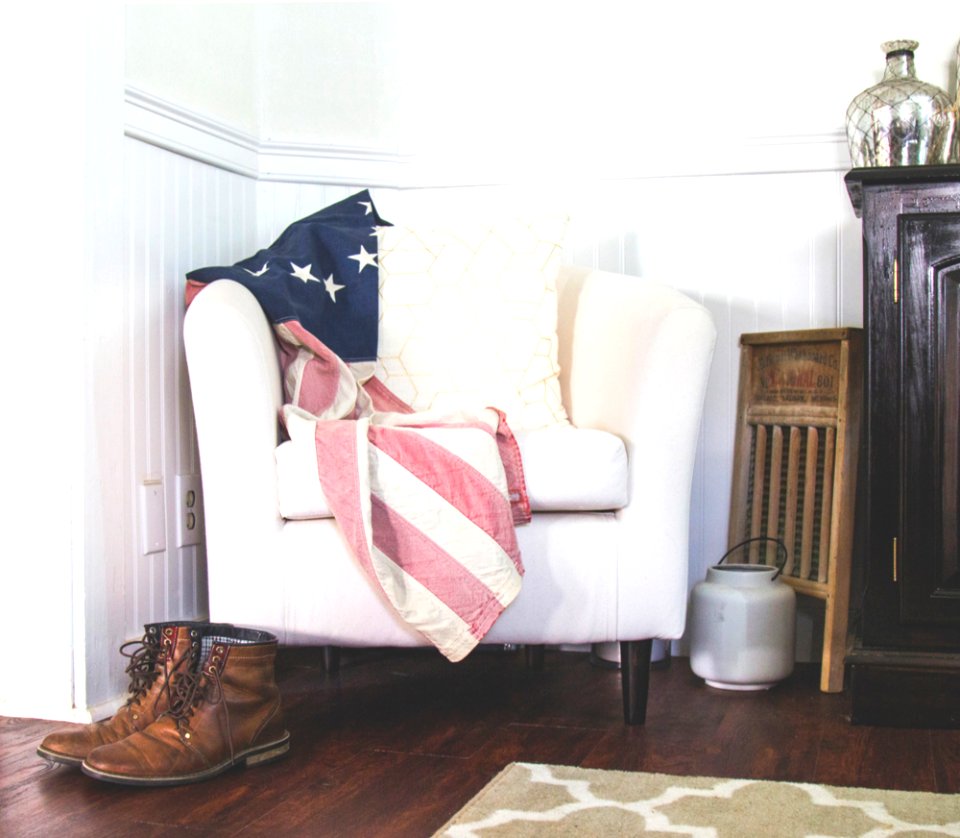 US flag and white throw pillow on white fabric sofa chair in room