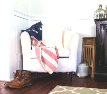 US flag and white throw pillow on white fabric sofa chair in room