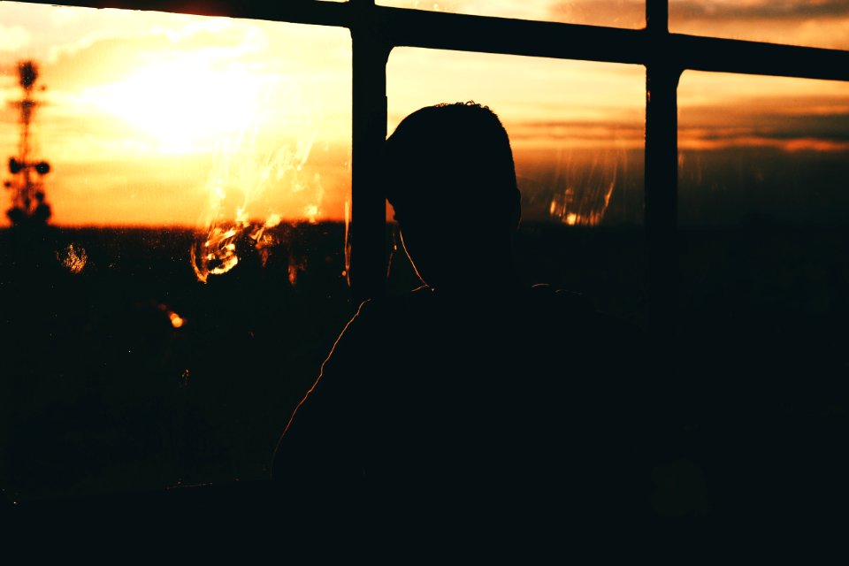 silhouette of a person by a glass window during sunset
