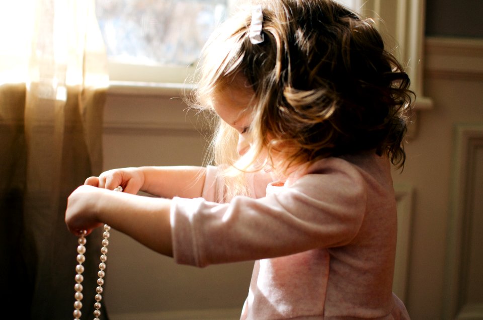 girl holding white pearl necklace inside room