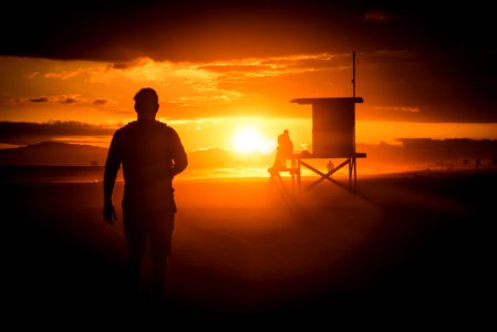 silhouette of man standing near wooden shed during sunset photo