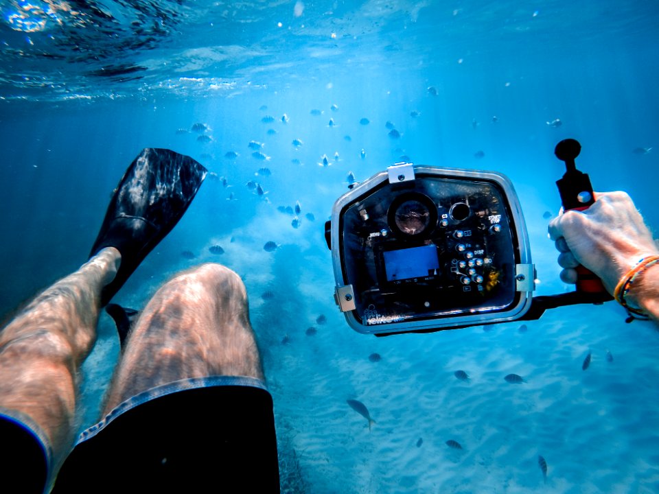 man bathing under the sea while holding black camera