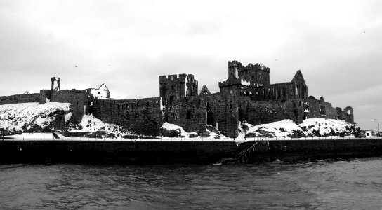 grayscale photo of concrete castle beside sea photo