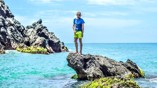 man in blue t-shirt standing on gray rock on see photo