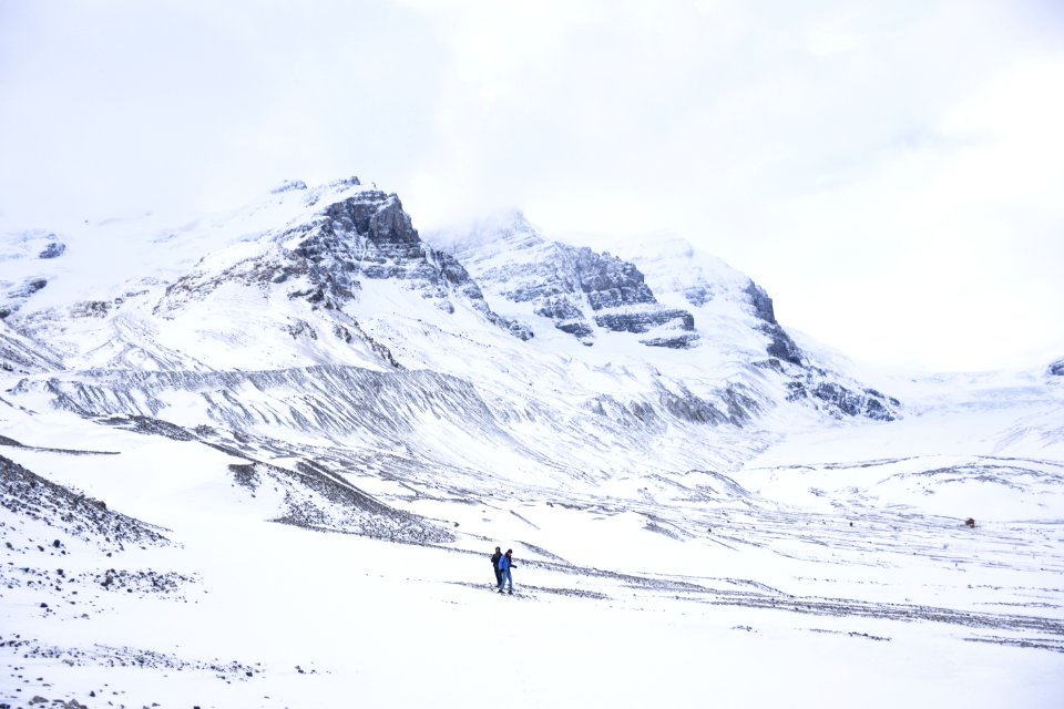 two person walking on snow covered ground next to mountains