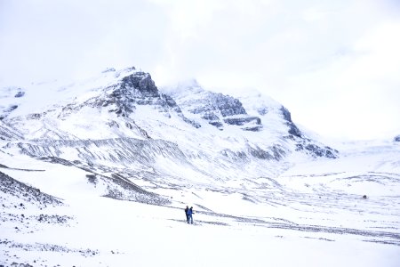 two person walking on snow covered ground next to mountains photo