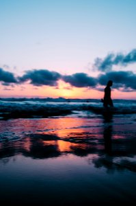 silhouette photo of a person walking on seashore under cloudy sky during golden hour photo