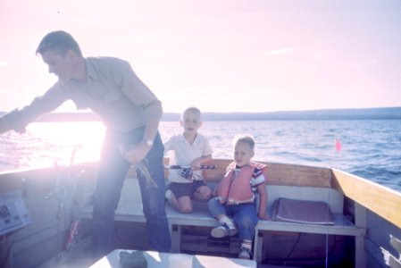 man holding gray fish standing beside two boys sitting on boat seats photo