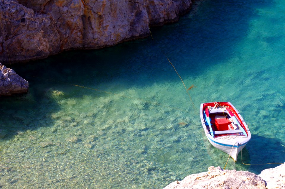 white and red boat toy docked on brown rock