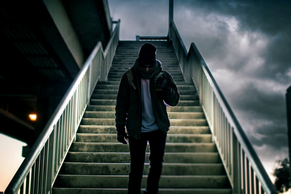 man wearing brown jacket walking on the stair under black sky