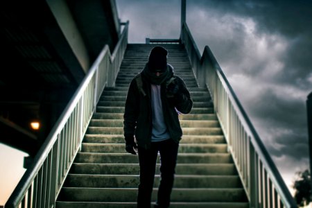 man wearing brown jacket walking on the stair under black sky photo