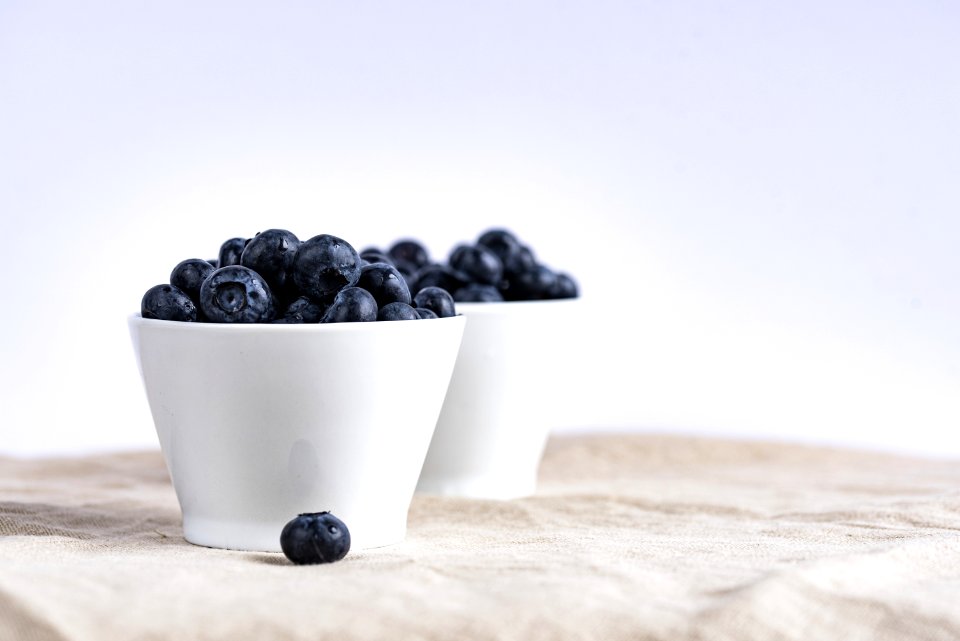 two white ceramic cup filled with blueberries fruit place on brown textile