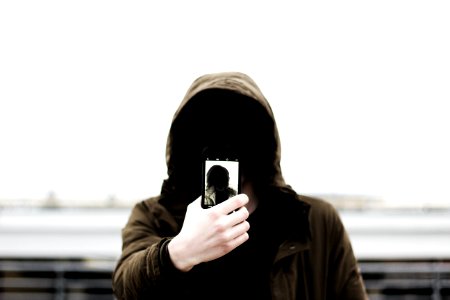 man wearing black hooded jacket and holding smartphone white taking close-up selfie photo
