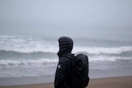 person wearing black duffle coat facing body of water photo