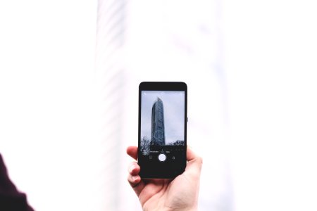 shallow focus photography of person taking picture of glass tower at smartphone photo