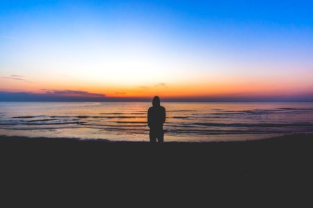 silhouette of person standing near sea during golden hour photo