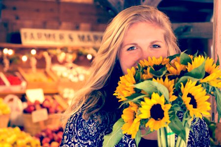 woman in blue and white floral top holding sunflower buoquet photo