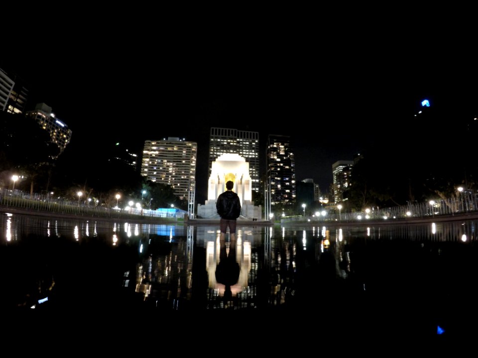 A man wearing a backpack and standing inside a city fountain.