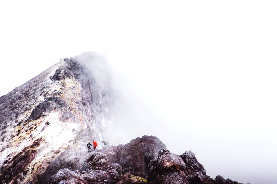 two people standing on mountain slightly covered with fogs during daytime