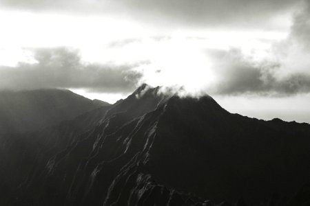 A black and white photo capturing the sun rising over a mountain in Hawaii.