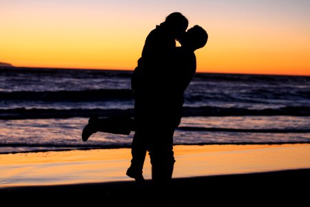 silhouette photo of couple kissing near sea during golden hour photo