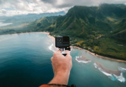 person holding black action camera fronting green mountains photo