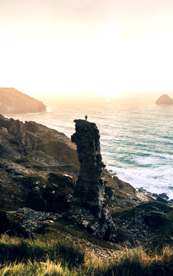 man standing on rock cliff near body of water