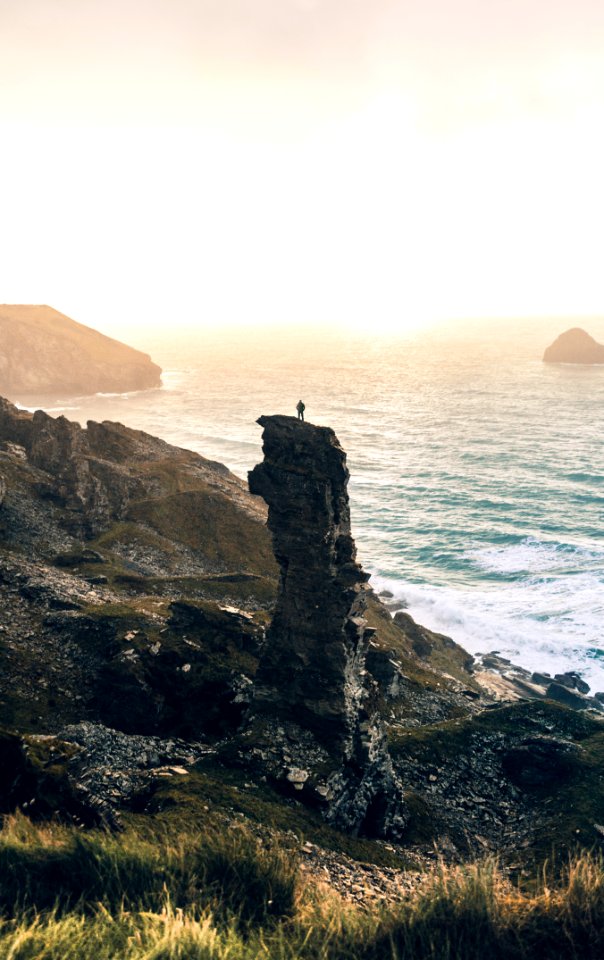 man standing on rock cliff near body of water photo