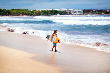 man carrying yellow and white surfboard standing near beach photo
