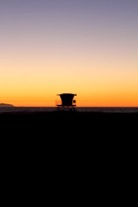 silhouette photo of shed on sand near sea during golden hours photo