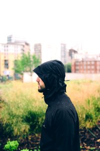 man wearing hoodie standing near grass with building background during daytime photo