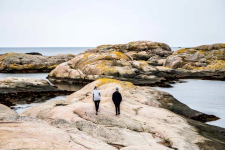 woman and man walking on rock formation near body of water during daytime photo
