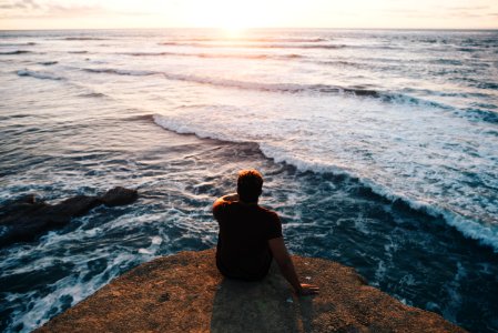 person sitting on cliff facing body of water