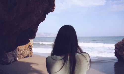 woman sitting under rock facing sea photo