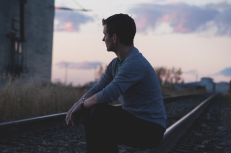 man sitting on railway under gray sky photo