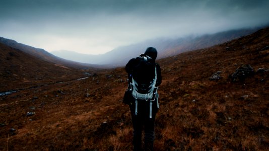 man carrying hiking bag standing under cloudy sky photo
