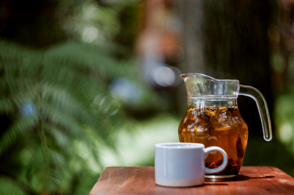 full glass of clear glass pitcher beside white ceramic teacup