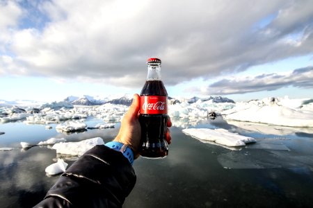 person showing photo of bottle of coke in front of icebergs photo