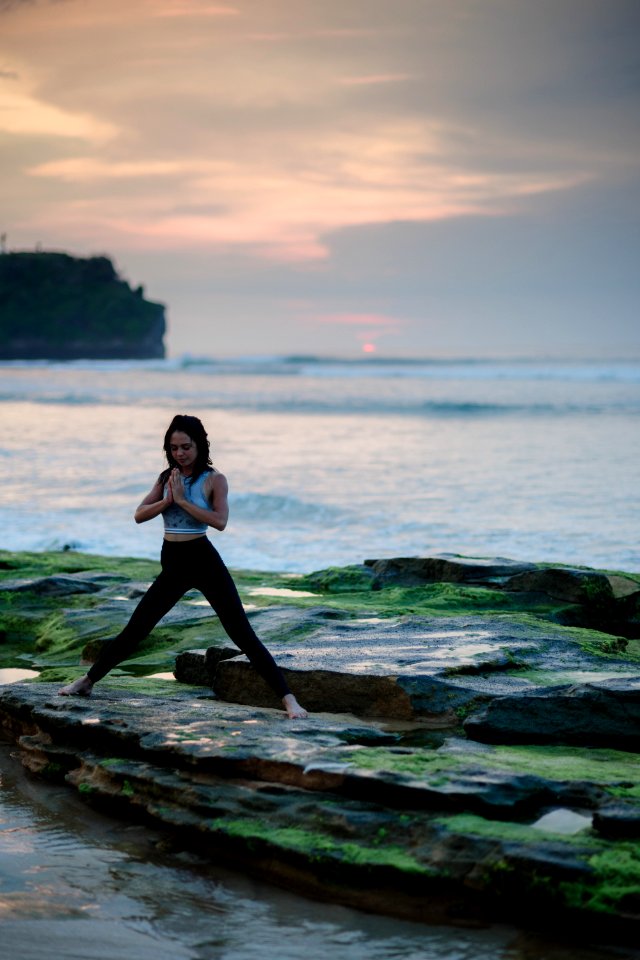 woman doing yoga on rock platform next to body of water