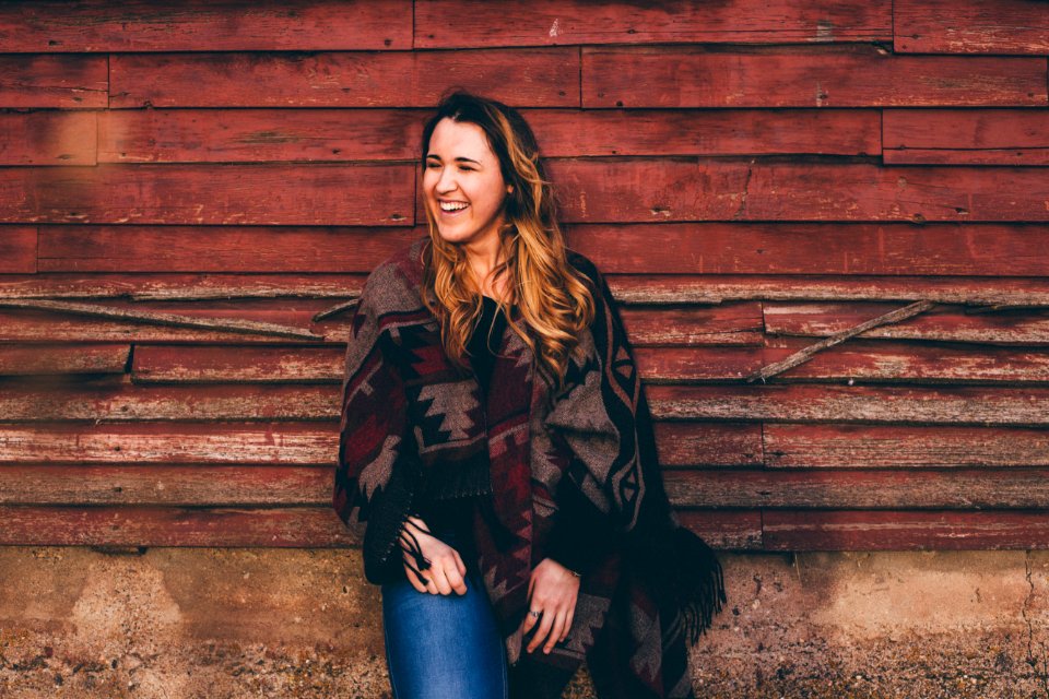 smiling woman wearing brown and black poncho leaning on wall