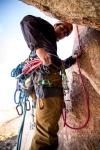 rock climber holding red rope strapped on waist while on side of brown boulder at daytime photo